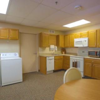 A kitchen interior featuring wooden cabinets, a stove, microwave, and a washer.
