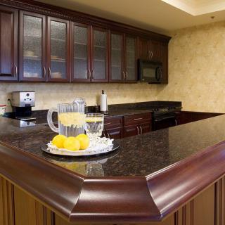 A modern kitchen with dark wood cabinets and a granite countertop, featuring a glass pitcher with orange juice and lemon slices.