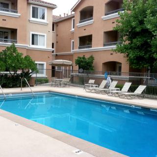 An outdoor swimming pool surrounded by an apartment complex with deck chairs and trees.