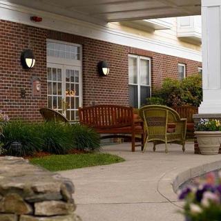 A comfortable outdoor patio with wooden benches and chairs in front of a brick building.