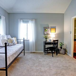 A cozy bedroom featuring a daybed and a small desk, with natural light streaming through the windows.