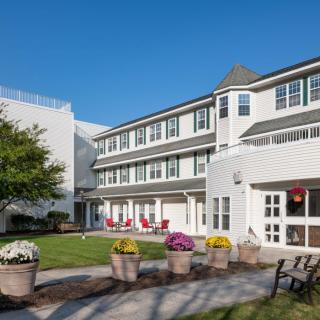 A white multi-story building with a patio area featuring red chairs and potted flowers.