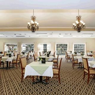 An elegant dining room with tables and chairs arranged neatly under ornate chandeliers.
