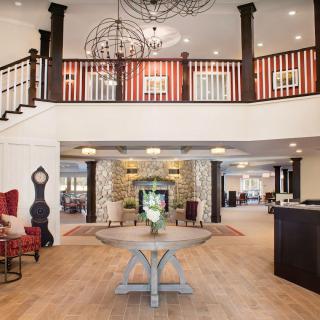 A spacious hotel lobby with elegant chandeliers, a grand staircase, and cozy furniture surrounding a fireplace.