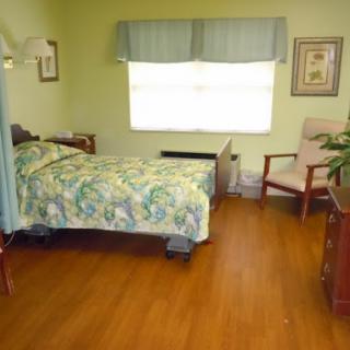 A cozy hospital room featuring a bed with colorful bedding, a chair, and natural light streaming through the window.