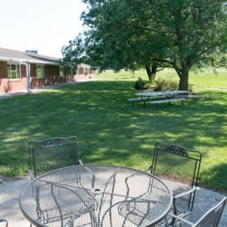 A peaceful outdoor patio area with a metal table and chairs overlooking a grassy lawn and trees.