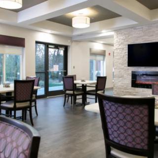 A modern dining area with elegant seating, large windows, and a wall-mounted television.