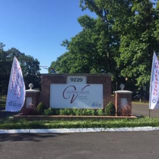 An outdoor entrance sign with banners on either side, surrounded by greenery and trees.