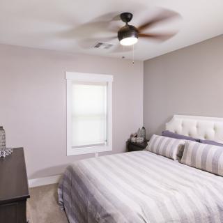 A minimalist bedroom with a neatly made bed, neutral color scheme, and a ceiling fan.