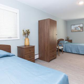 A cozy bedroom featuring two beds with blue bedding, a wardrobe, and a nightstand, perfectly designed for comfort and relaxation.