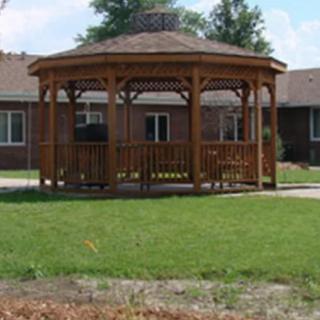 A wooden gazebo in a grassy area with houses in the background.