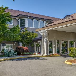 A well-maintained building entrance with surrounding greenery and a driveway.
