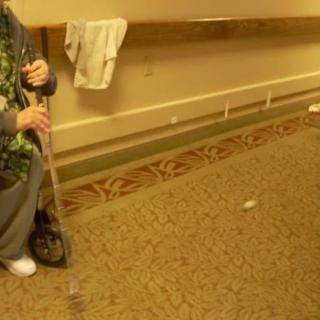 Elderly person with a walking stick in a hallway.
