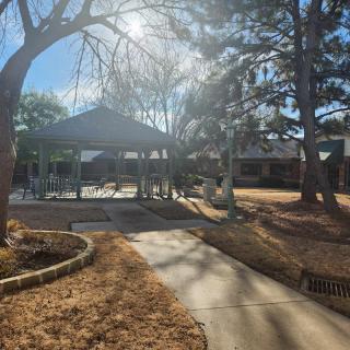 A sunny day in the park featuring a gazebo and a pathway surrounded by trees.