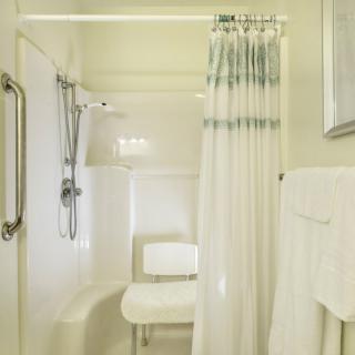 An accessible bathroom with a shower chair and grab bars.