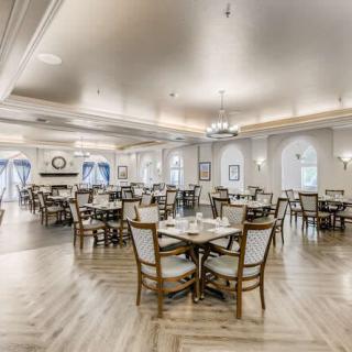 An elegantly designed dining area with multiple tables and chairs, featuring chandeliers and a wooden floor.