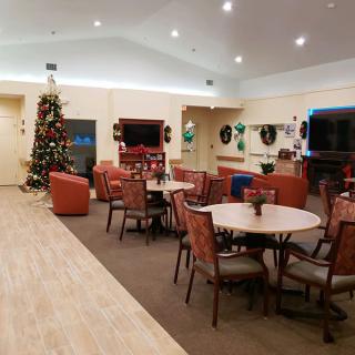 A cozy lounge area decorated with Christmas decorations, featuring tables and chairs, a television, and a festive tree.