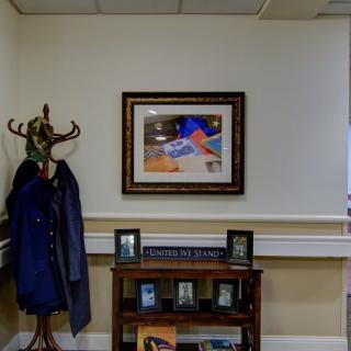 Office interior with a coat rack, framed artwork, and a shelf displaying photos.
