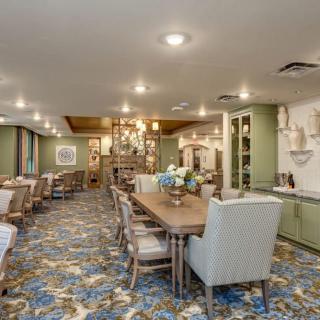 A spacious dining area with elegant chandeliers, floral carpet, and neatly arranged tables and chairs.