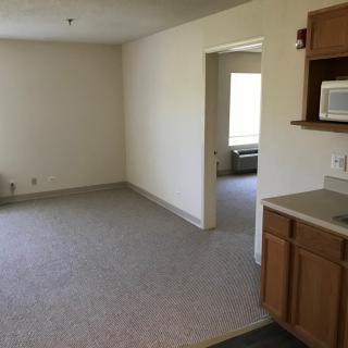 An empty apartment with a small kitchen area and living room.