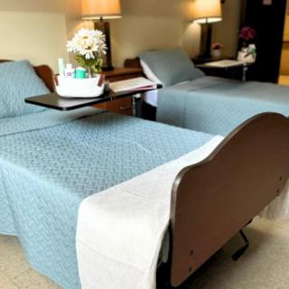 A clean and organized hospital room with two beds, equipped with tray tables and lamps.