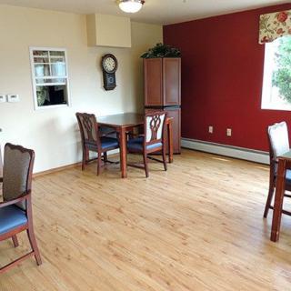 A cozy dining area with wooden floors, several tables and chairs, and a window letting in natural light.