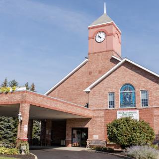 A charming brick building featuring a clock tower and inviting entrance, surrounded by well-maintained landscaping under a clear blue sky.