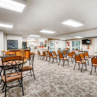 A spacious dining area with multiple tables and chairs, featuring a patterned carpet and modern ceiling lighting.