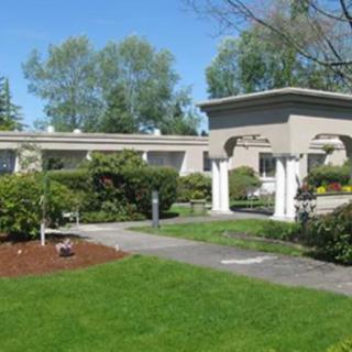 A small, single-story building surrounded by a well-maintained garden and pathway on a sunny day.
