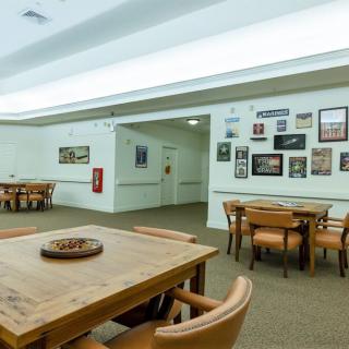A dining area with wooden tables and chairs, adorned with wall art and illuminated by overhead lighting.