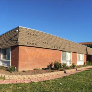 A brick building with a sloped roof on a sunny day, surrounded by grass and a small garden.