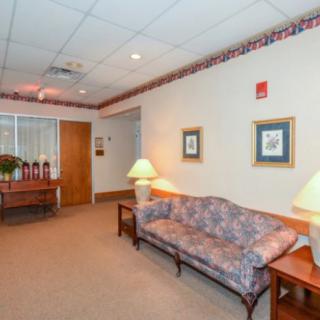 A cozy waiting room with a floral sofa, two lamps on side tables, and framed artwork on the walls.