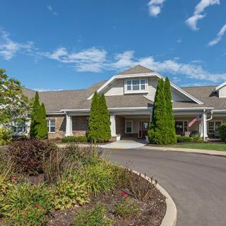 A modern building with landscaped gardens and a curved driveway under a clear blue sky.
