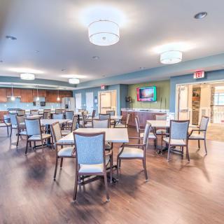 A spacious and well-lit dining area with several tables and chairs, featuring a modern interior design with wooden flooring.