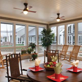A cozy veranda with a dining area, rocking chairs, and large windows.