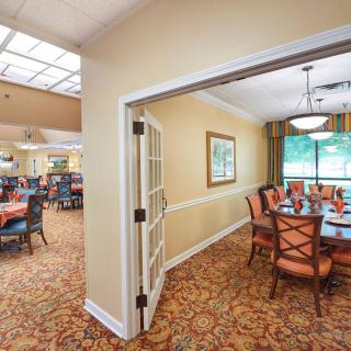 A beautifully decorated dining area with a large table and chairs, featuring carpeted floors and natural lighting from a window.