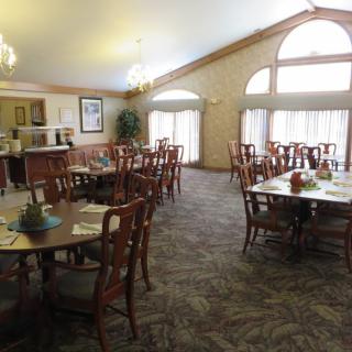 An elegant dining room with neatly arranged tables and chairs, illuminated by natural light from large windows.