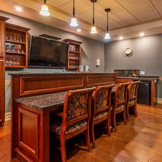 A cozy home bar with elegant wood furniture, counter seating, and a mounted television.