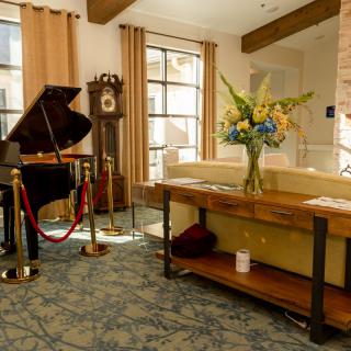A cozy living room featuring a grand piano, grandfather clock, and elegant floral arrangement.