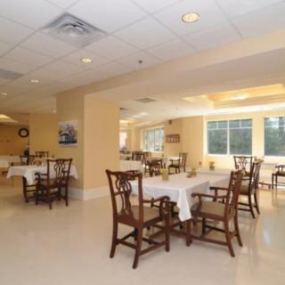 An empty dining room with tables and chairs arranged neatly, illuminated by natural light from large windows.