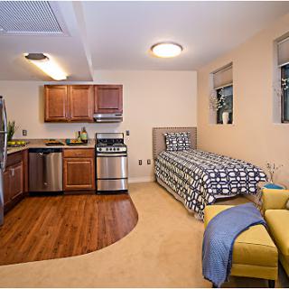 A cozy studio apartment featuring a kitchen area and a single bed, designed for efficient living.