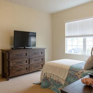 A cozy bedroom with a bed, dresser, and television by the window.