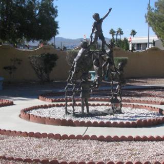 A bronze sculpture of people in a garden setting under a clear blue sky.