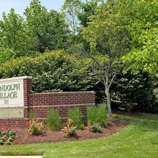 Entrance sign with brick structure surrounded by trees and landscaping.