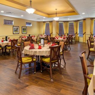 A cozy restaurant dining area with neatly arranged tables and chairs, featuring warm yellow walls and elegant wooden flooring.