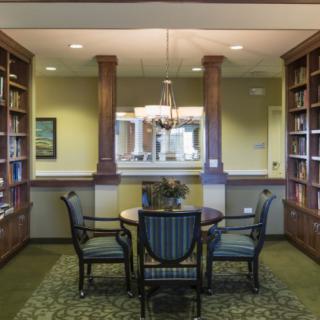 A cozy library reading area with wooden bookshelves, a round table, and elegant chairs.
