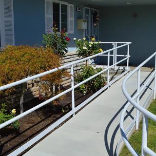 An accessible ramp with handrails leads to the entrance of a building, surrounded by a small garden.