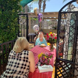 An outdoor birthday celebration with balloons, flowers, and a cake on the table.