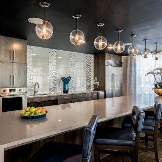 A modern kitchen featuring a long countertop with bar seating and stylish globe pendant lights.