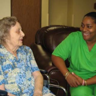 An elderly woman in a wheelchair having a friendly conversation with her caregiver.